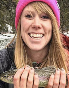 Anna Crider, member of the Advisory Council, smiles holding a fish along the river